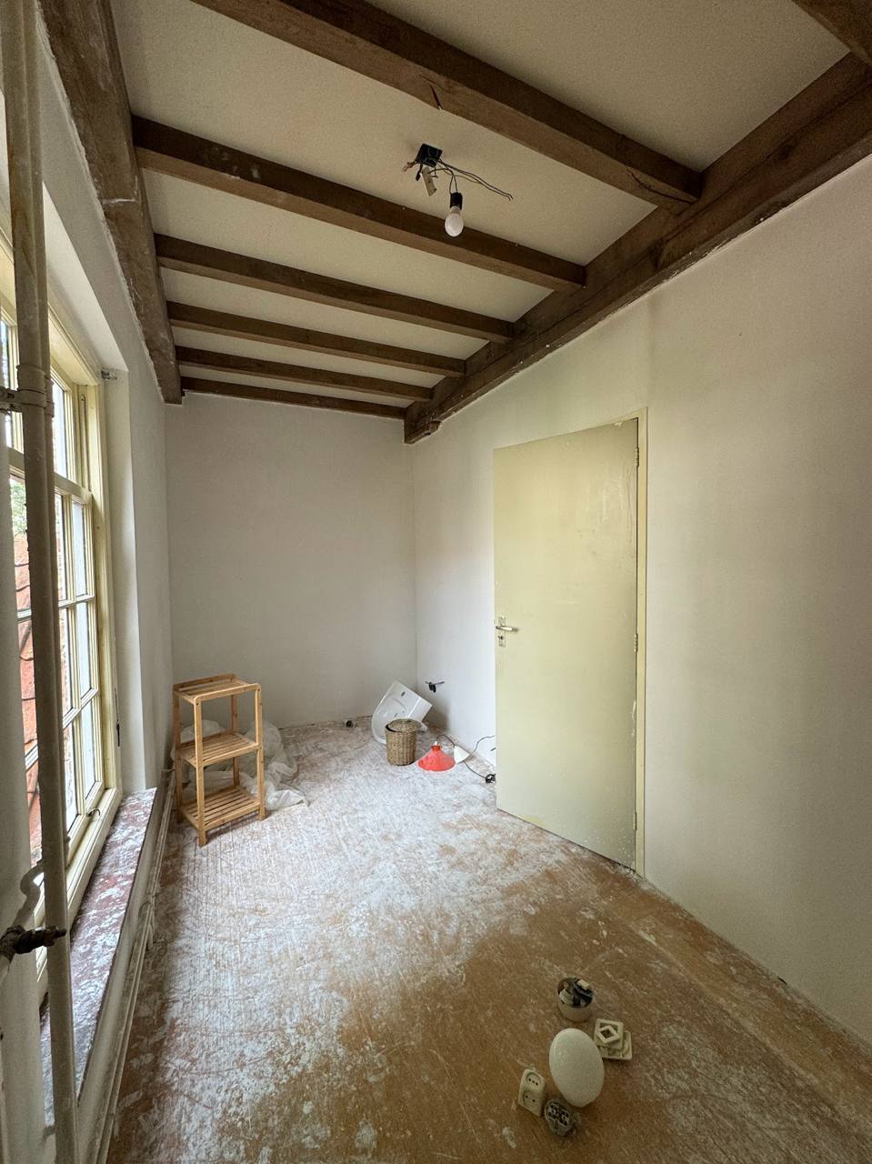 Renovated room with plastered walls, painted door and exposed wooden ceiling beams