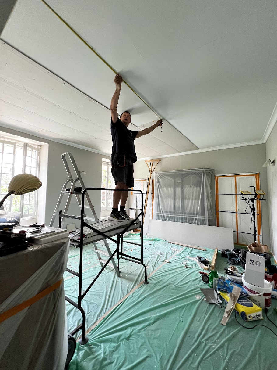 Worker installing plasterboard ceiling panels on a platform in a protected room