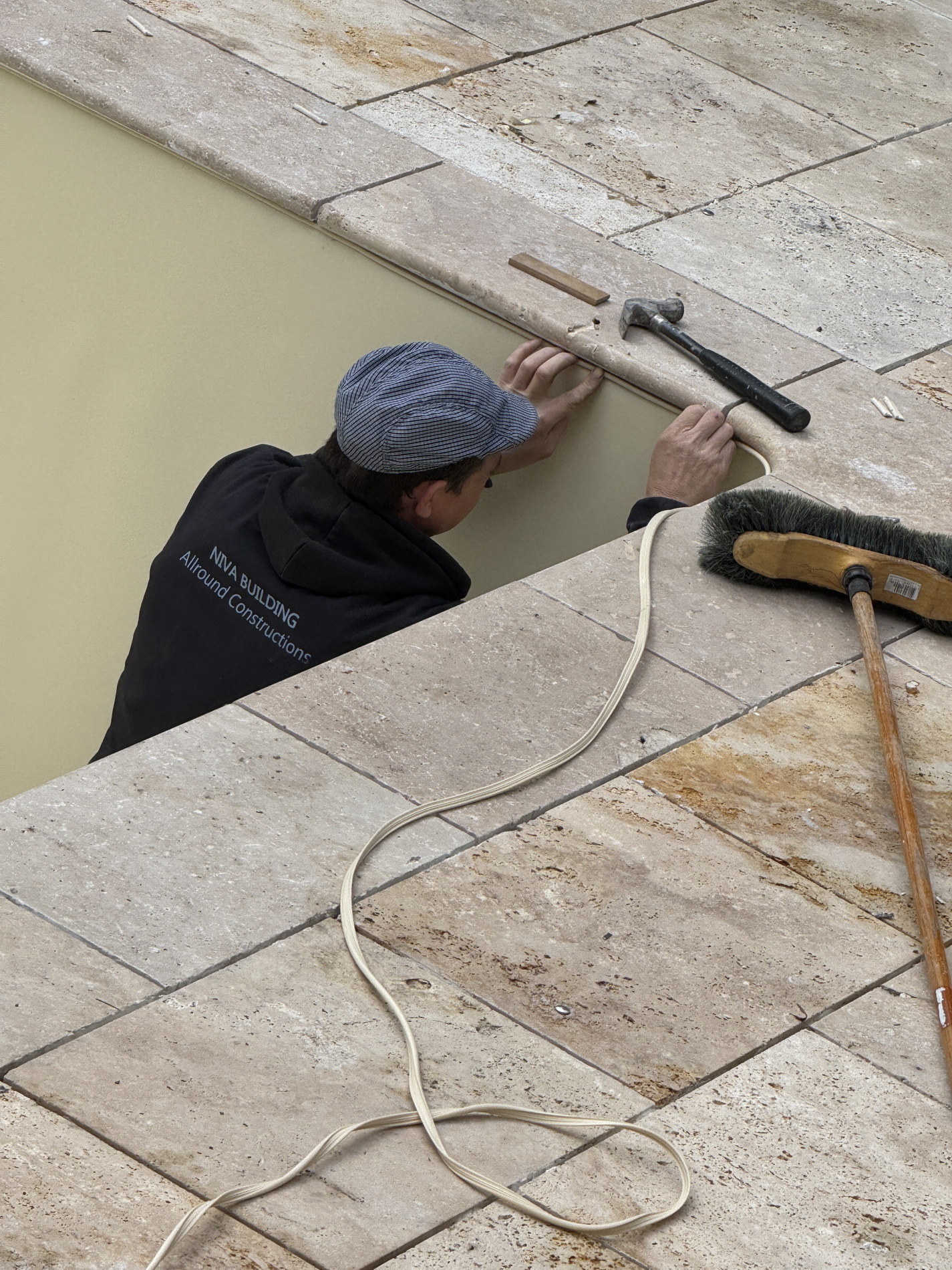 Close-up of a worker fitting stone coping on a pool edge with tools nearby