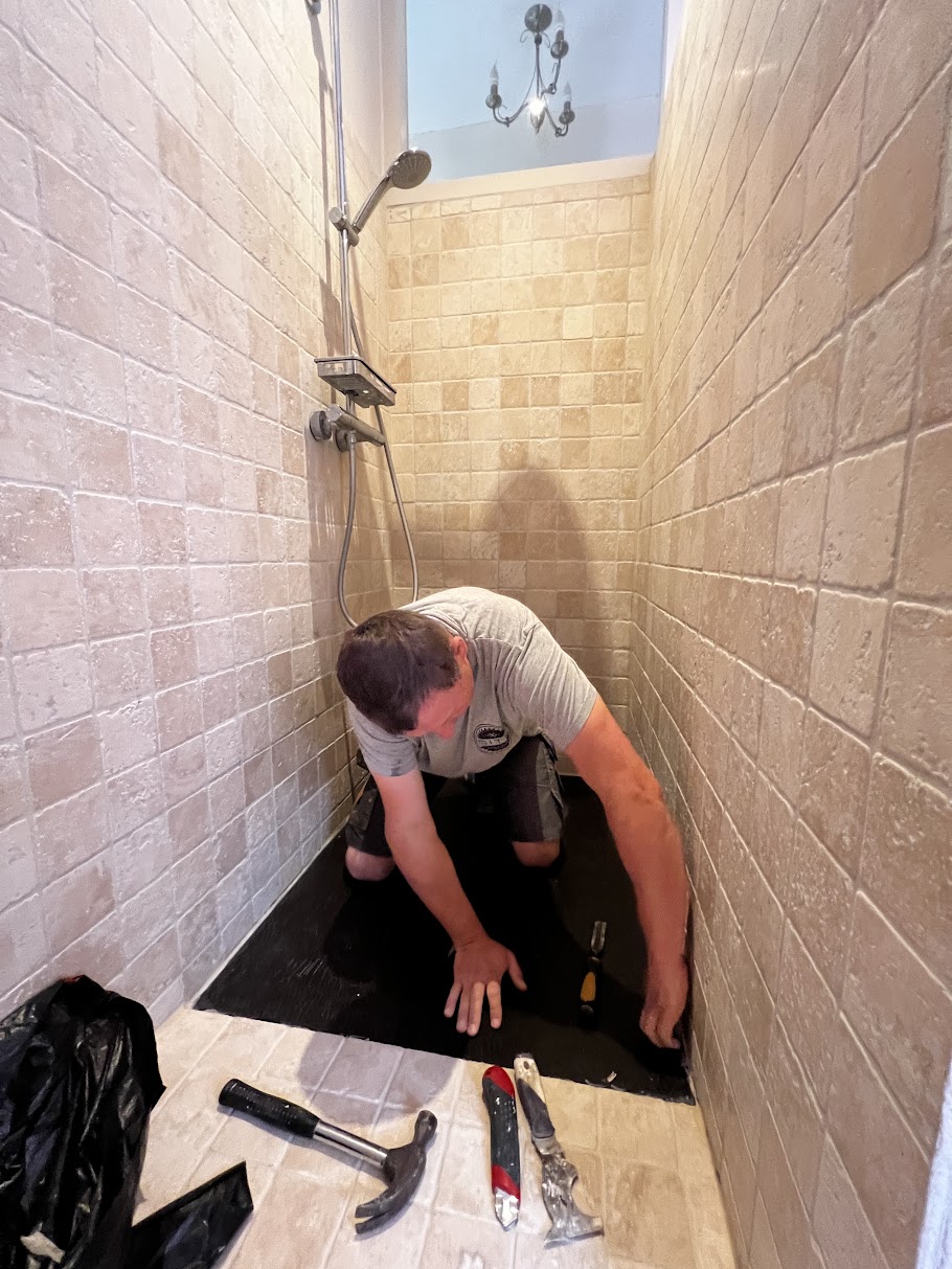 Tiler installing beige brick-pattern wall and floor tiles in a narrow shower