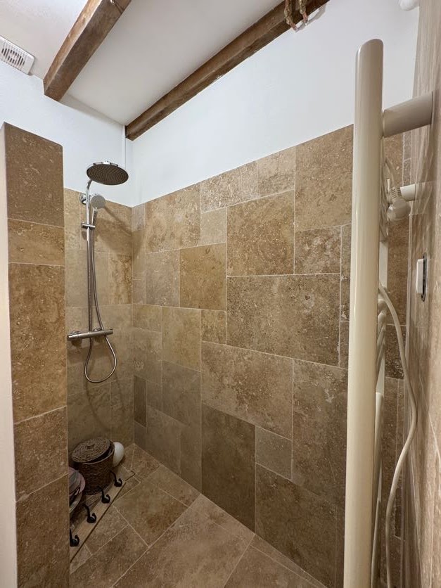 Compact beige tiled shower with matching floor and exposed timber ceiling beams