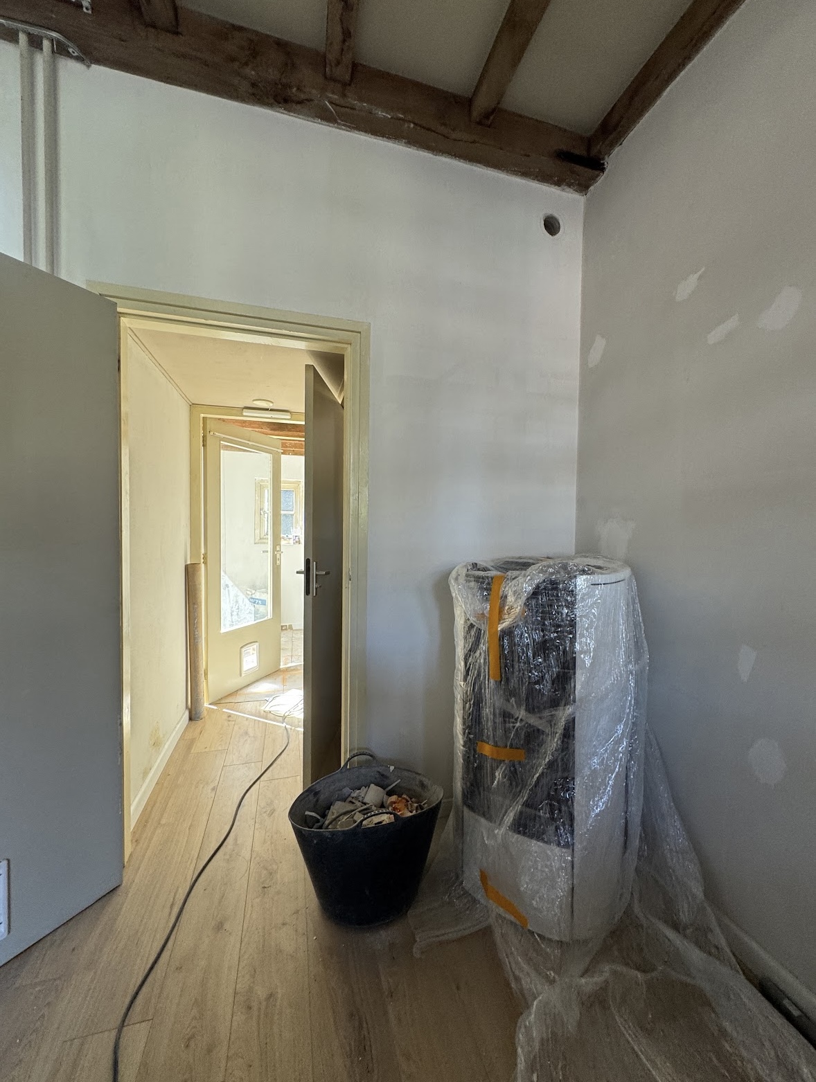Hallway with freshly plastered walls, protected appliances and exposed wooden beams