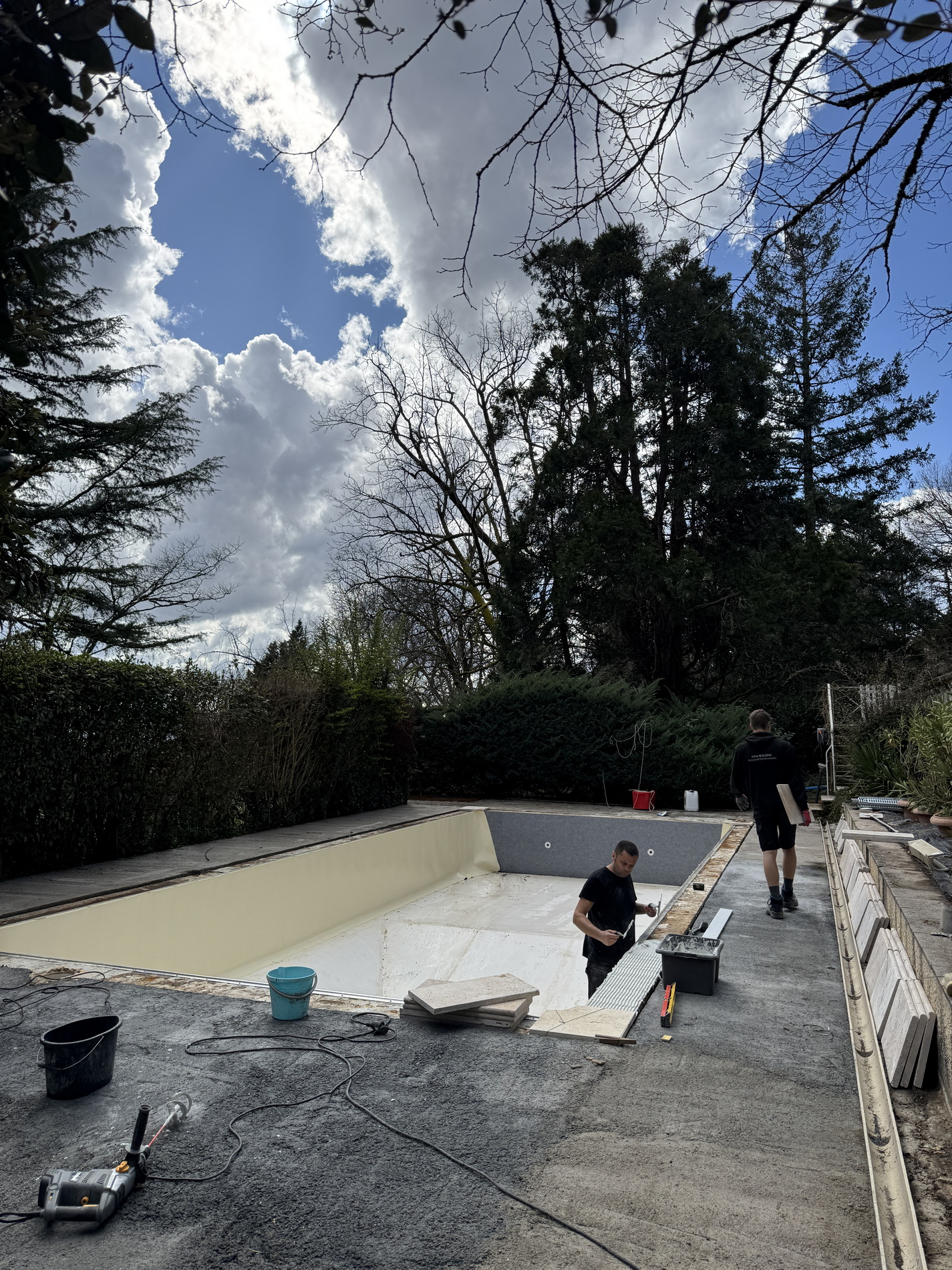 Workers preparing an empty swimming pool for new lining and coping installation