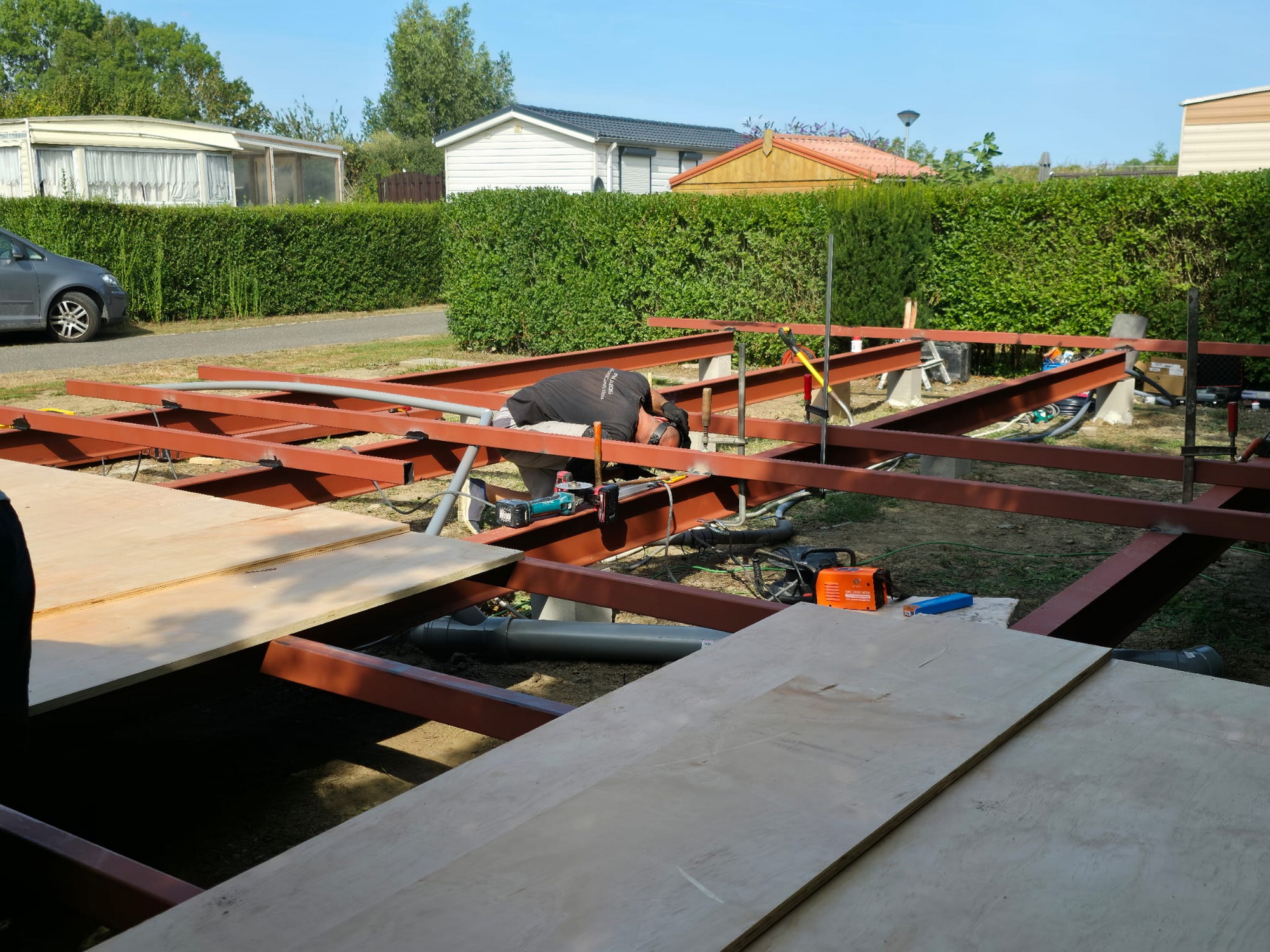 Worker on the steel frame installing boards with utility pipes routed below the floor