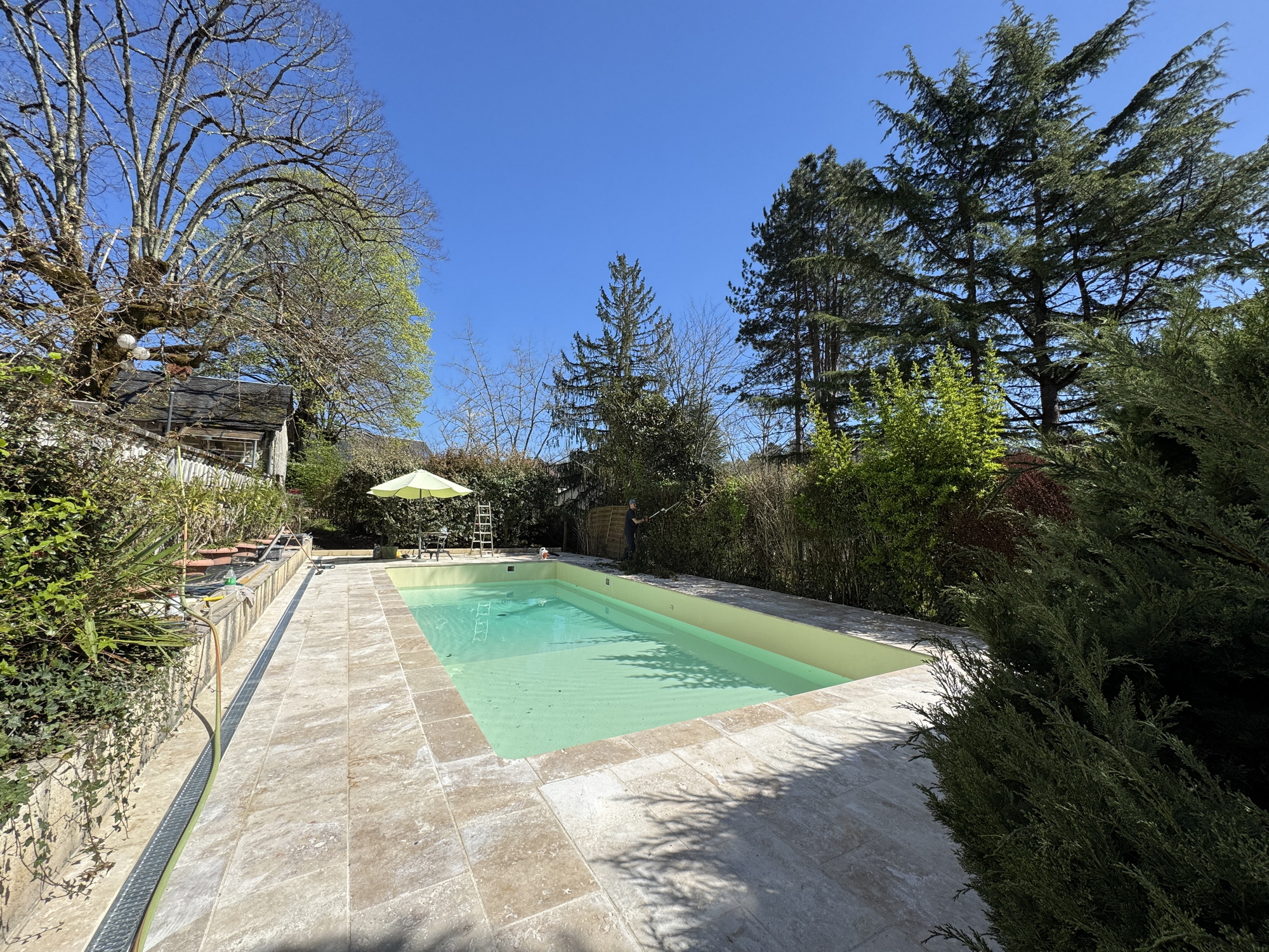 Completed renovated swimming pool filled with water and surrounded by new stone terrace
