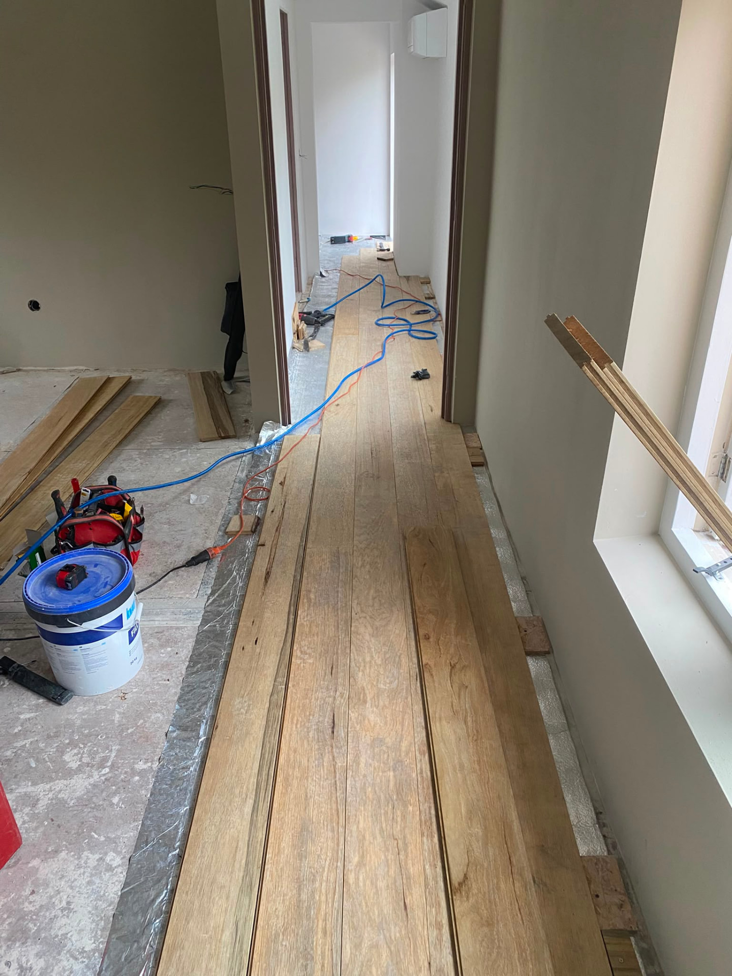 Long residential corridor with new light wood plank flooring partially laid