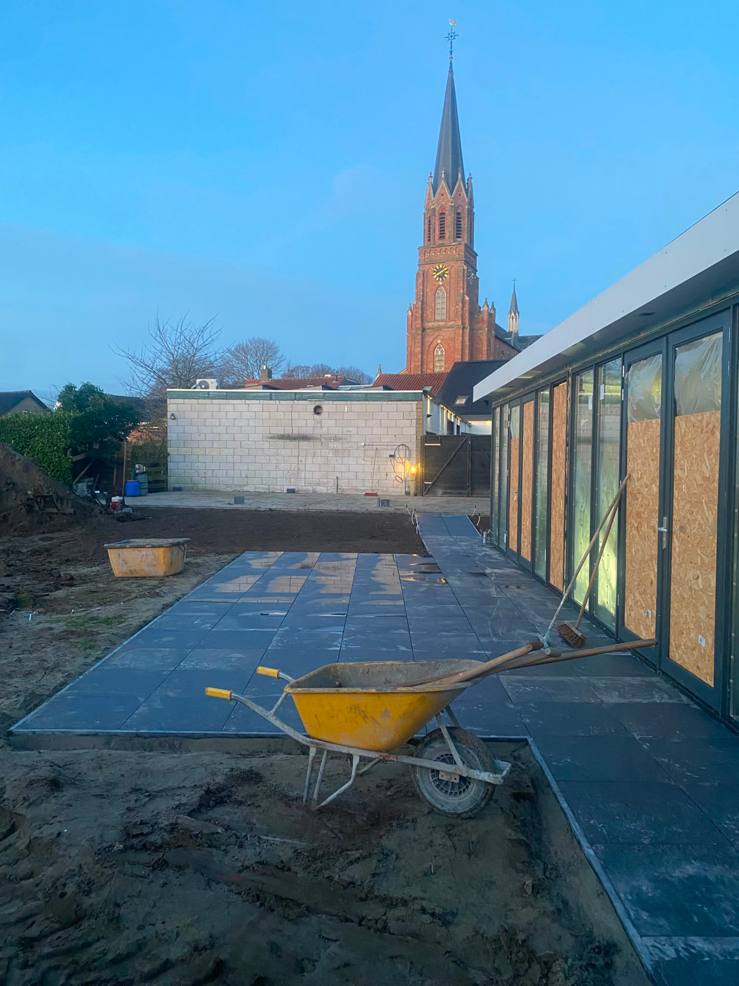 Outdoor patio construction site with large dark pavers and church tower in background