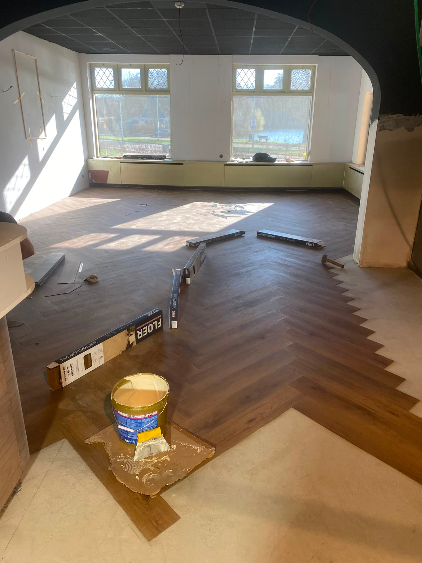 Sunlit hall with partly installed dark herringbone flooring and paint supplies