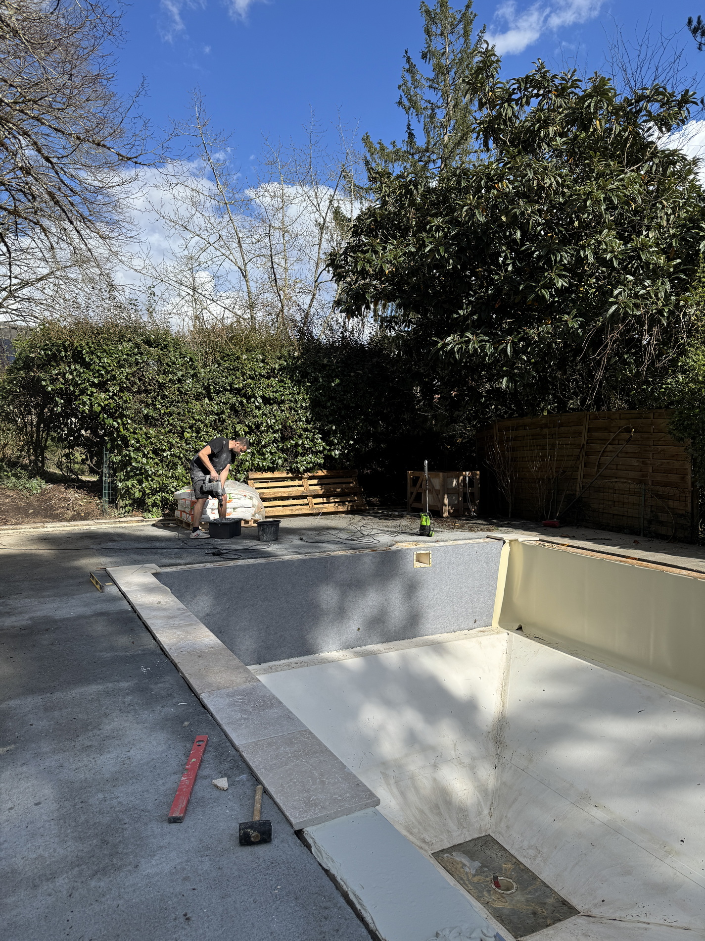 Worker laying stone coping tiles along the edge of a renovated swimming pool